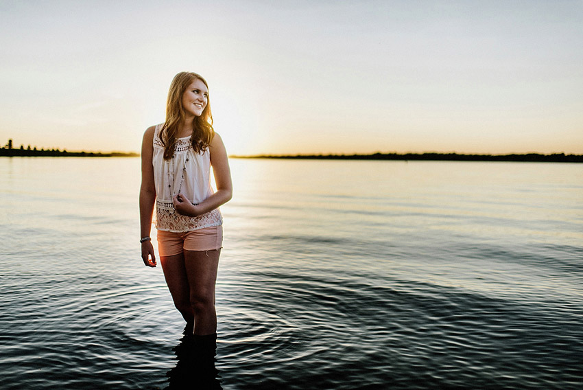 senior girl standing in a lake at sunset with ripples