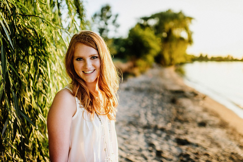 senior girl under a willow tree standing next to a lake