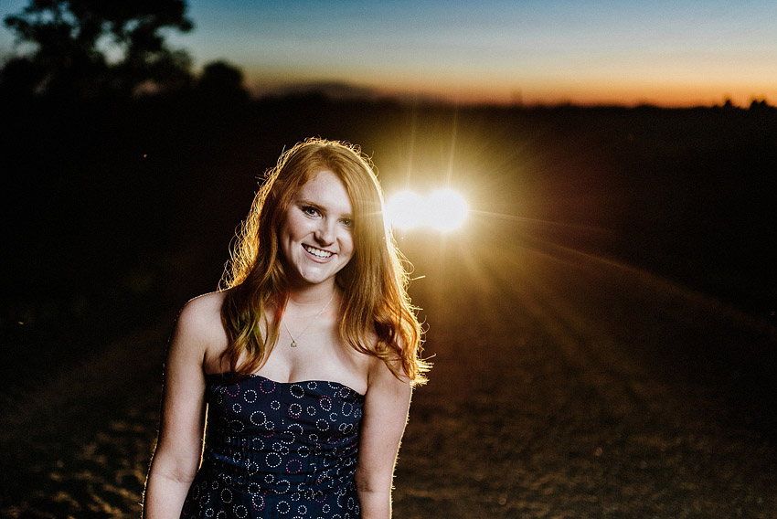 redhead senior girl on a country road with headlights behind