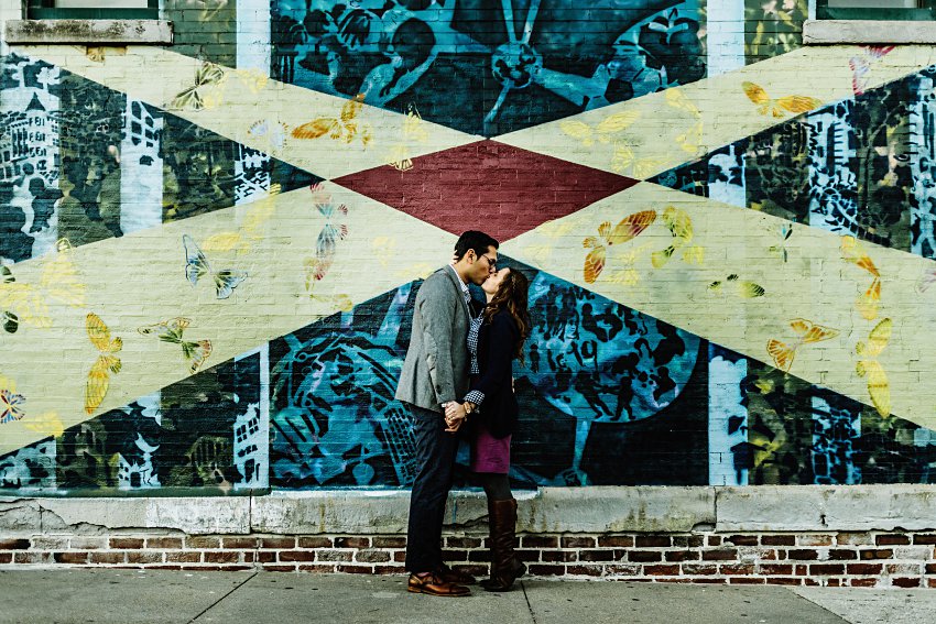two people kissing and holding hands in front of a mural