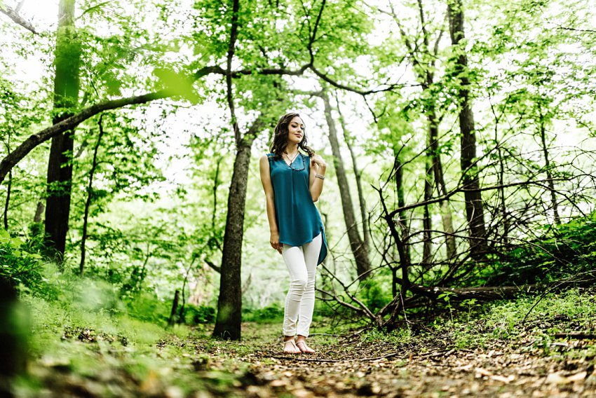 girl in white pants and a blue top standing in a clearing in the woods