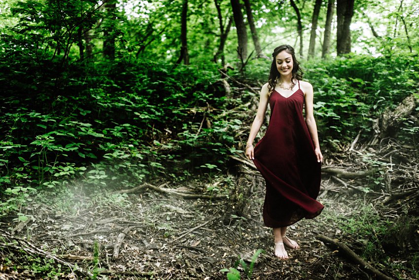 smiling girl in the woods with light behind her while she swings her dress with smoke on the ground