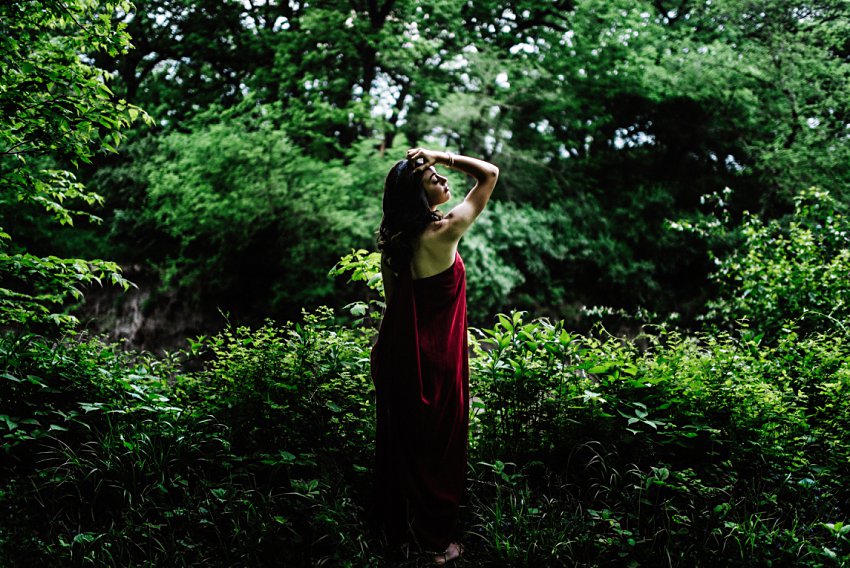 full length photo of a girl in a forest clearing looking very serious off camera with her hand in her hair