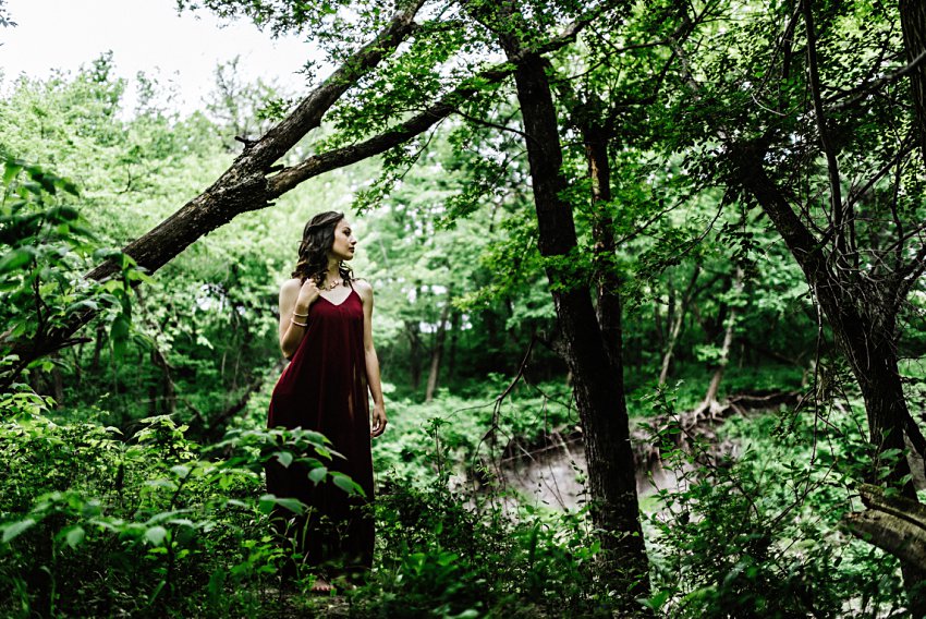 girl in a red dress looking off camera in a dramatic view of the woods