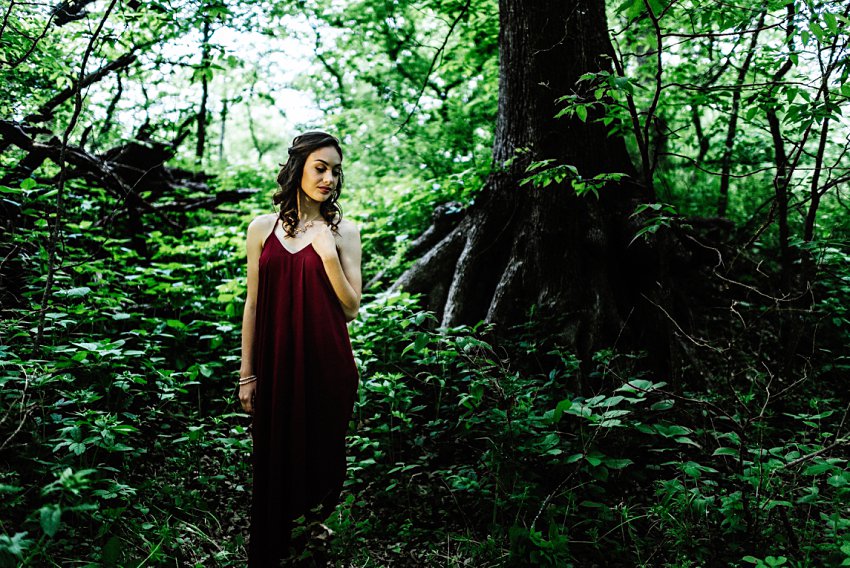 girl standing in dramatic light in front of tree roots holding her necklace
