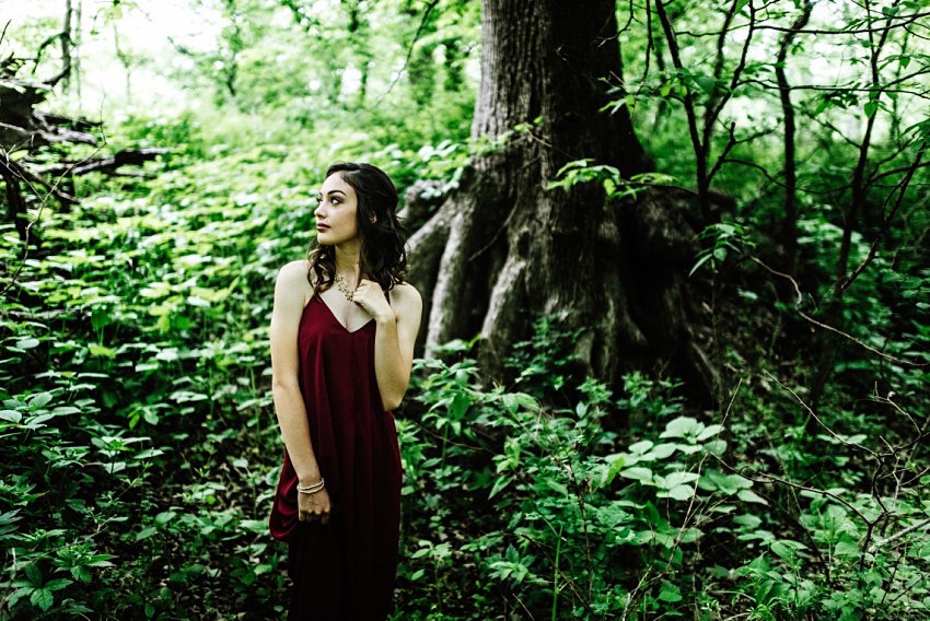 girl standing in front of tree roots holding her necklace