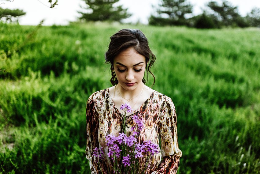 girl in a field looking down at purple flowers