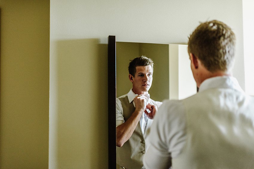 the groom adjusting his tie in a mirror