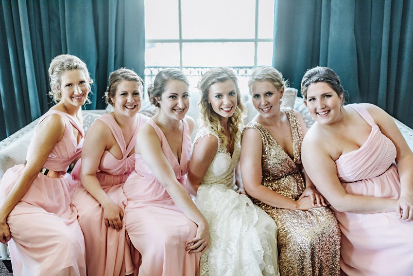 the bride and bridesmaids sitting together on a couch in front of a big window