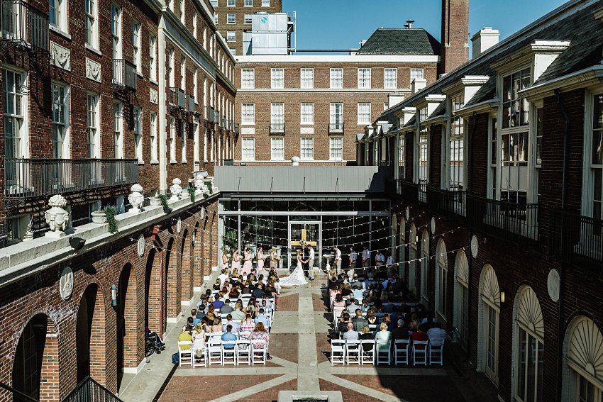 the bride and groom standing in the courtyard at their wedding with all of their guests seated watching them