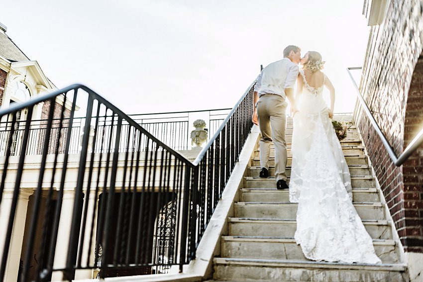 bride and groom exiting up the stairs into the sun while kissing