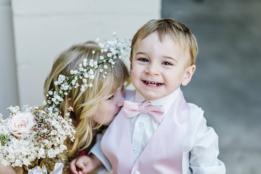flower girl giving the ring bearer a kiss while he smiles