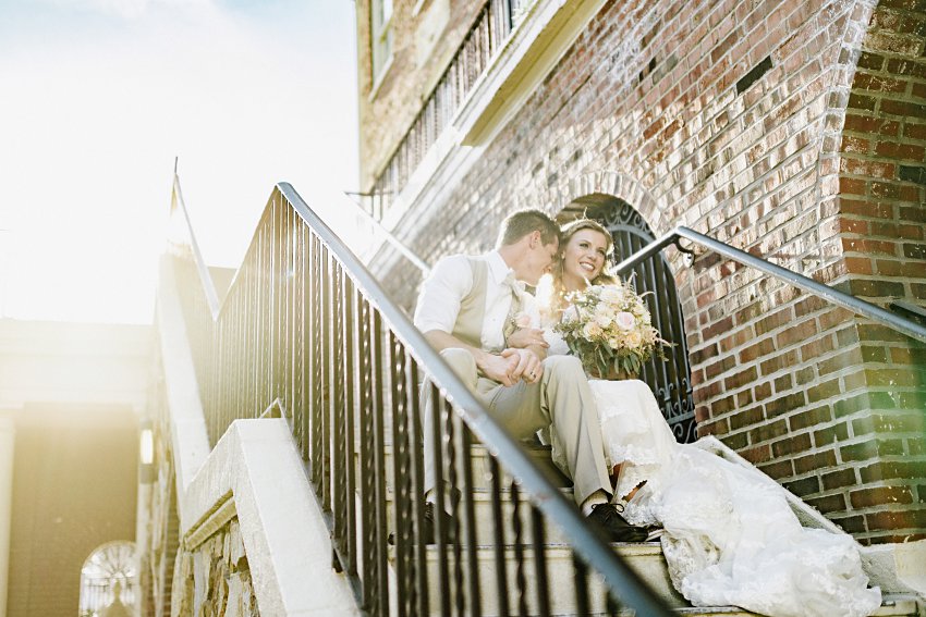the groom nuzzling the bride's cheek while they sit on the stairs in the sunlight