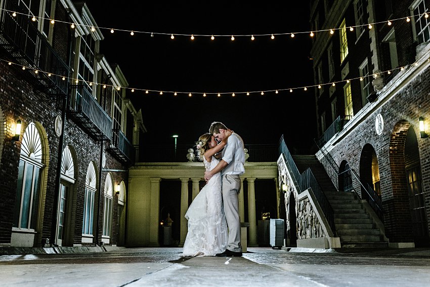 a bride and groom standing in a courtyard at night holding each other close