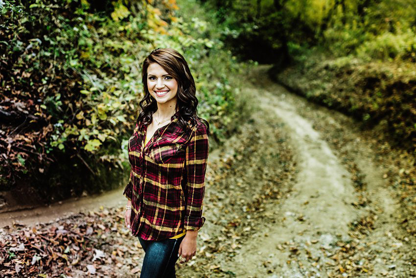 girl in a flannel standing on a path in the woods in the fall