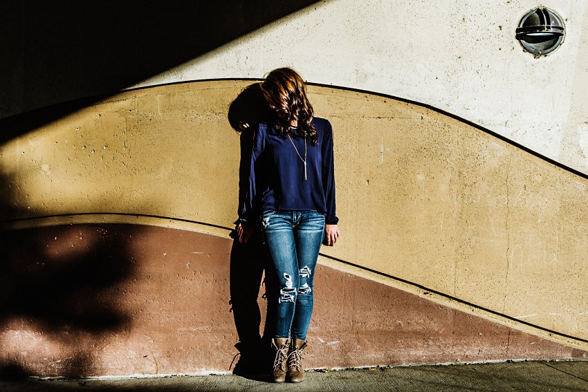 girl in a blue top and jeans standing in front of a decorative concrete wall with a shadow overhead