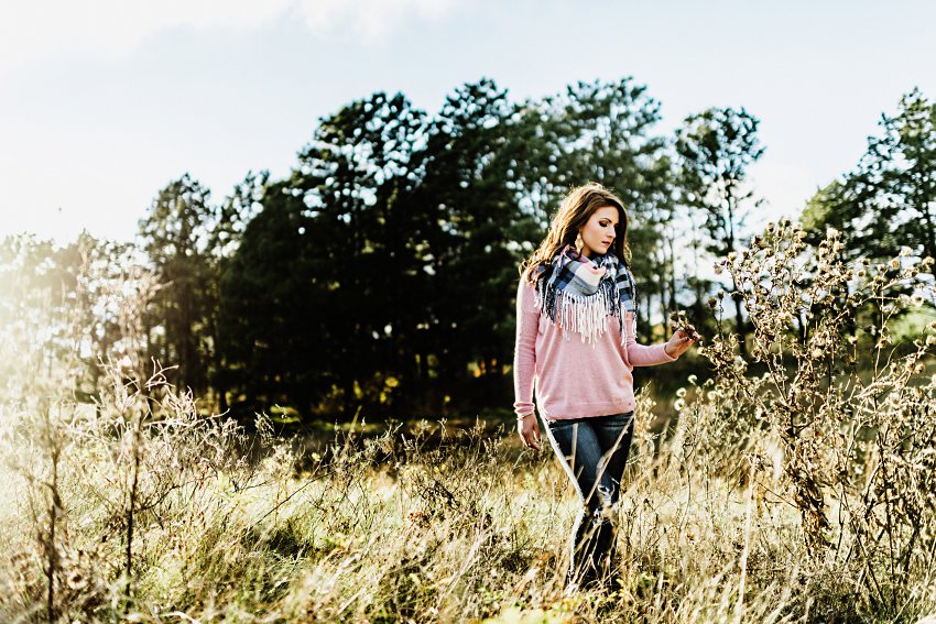 girl in a pink sweater and scarf walking through the prairie and touching the plants