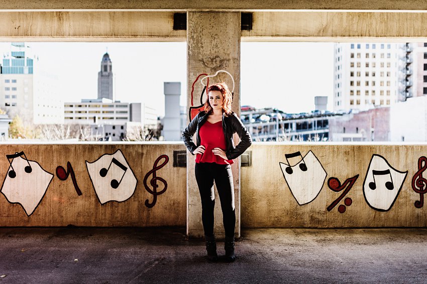 girl in red top and leather jacket standing in a parking garage with music graffiti in the background