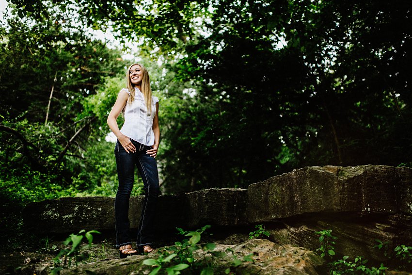 looking up at girl in a white top and black jeans standing on a rocky ledge