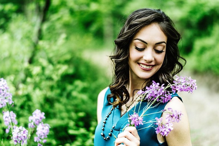 girl in white pants and a blue top looking at the purple flowers she's holding